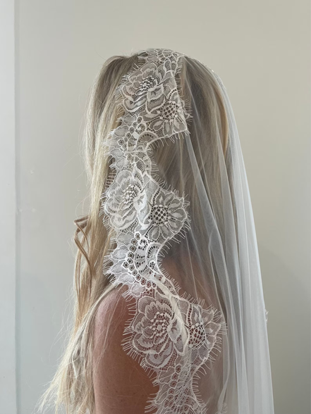 Chantilly Lace mantilla veil with floral patterns worn by a person with blonde hair against a plain background