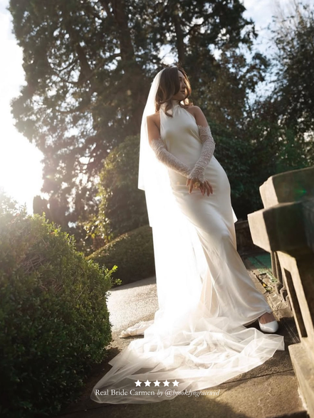 Real bride in a white wedding dress and Harriett Falvey double edged lace gloves standing outdoors with trees in the background