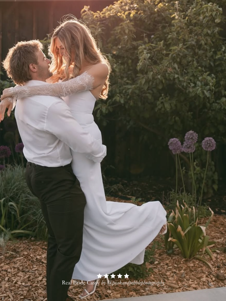 Man lifting a woman in a wedding dress and Harriett Falvey doubled edged lace gloves in a garden setting with greenery and flowers. And a five star review overlay.