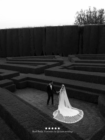 Black and white photo of a couple holding hands in a maze-like structure. Bride wearing her extra wide chantilly lace mantilla veil by Harriett Falvey.