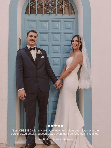 Man and woman in wedding attire standing in front of a blue door. Featuring her custom chantilly lace short mantilla veil by Harriett Falvey